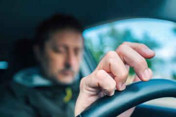 Nervous driver tapping fingers on car steering wheel while waiting