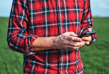 Closeup of male farmer's hands using mobile phone out in the field