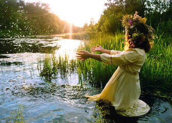 girl in flower wreath stand in river. sunny nature. summer background. Floral crown, symbol of...