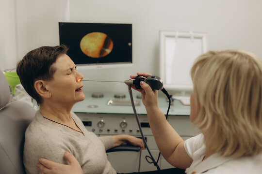 Nose endoscopy. Rhinoscopy procedure with rhinoscope. ENT doctor otolaryngologist with headlight treat nose woman patient