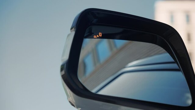 Turning on the blind spot warning BSW system on the side mirror of a car in a city traffic jam.