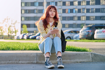 Young beautiful serious woman using smartphone, sitting on floor, urban style