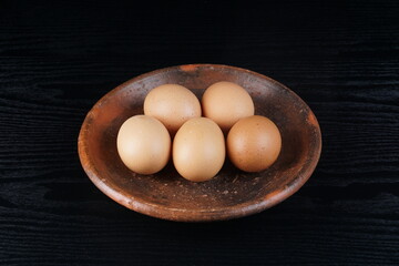chicken eggs on a clay plate on a black table with a black background with studio lighting