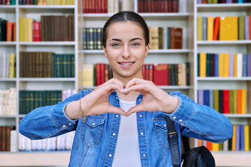 Happy teenage girl student showing heart gesture inside school building