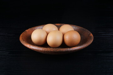 chicken eggs on a clay plate on a black table with a black background with studio lighting