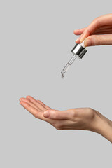 Clear serum dripping from a dropper on to your hand. Daily skincare and body care routine. Female hand holding  a dropper with cosmetic product on a light gray background. Close up.