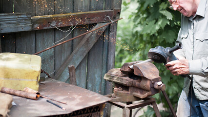 old man working. Cutting a metal pipe. spark. the pipe is clamped in a vice. man's hands hold a grinder. old iron vise, rusty pipe. electric tool, working with metal. Bulgarian, disc grinder