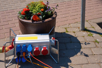 Portable electricity distributor on the sidewalk. Black and red electrical wires lie on the ground.