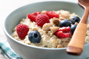 Oatmeal porridge with raspberries, blueberries and almonds in bowl on wooden table. Copy space