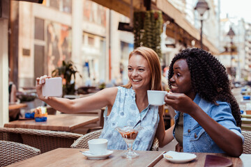 Two women taking selfie at outdoor cafe table
