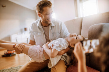 Father playfully lifting daughter in the living room