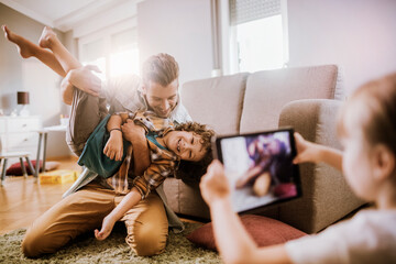 Father and son playing at home while daughter takes a picture