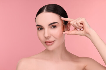Beautiful young woman holding skincare ampoule on pink background