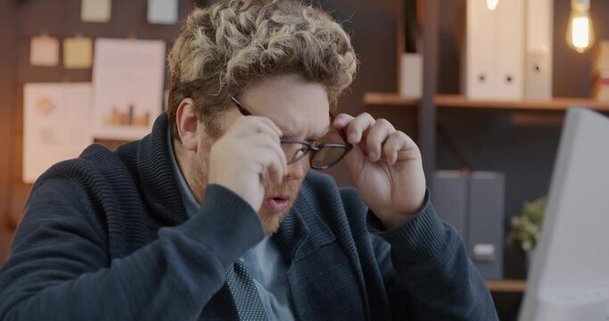 Loop of shocked businessman putting on glasses and staring at computer monitor in office in evening. Emotion and business person concept.