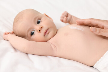 Woman applying body cream onto baby`s skin on bed, closeup