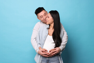 Man touching his pregnant wife's belly on light blue background