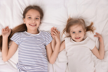 Cute little sisters on bed, top view