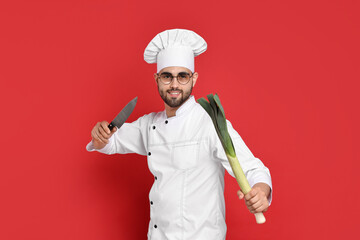 Professional chef with leek and knife having fun on red background