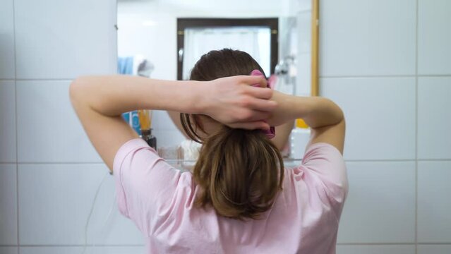 Cute teenager girl child doing a ponytail with hair tie looking in the mirror.