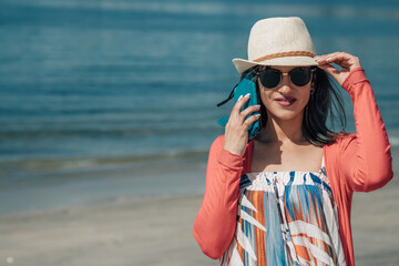 young tourist woman walking along the shore of the beach talking on the phone