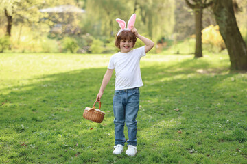 Easter celebration. Cute little boy in bunny ears holding wicker basket outdoors