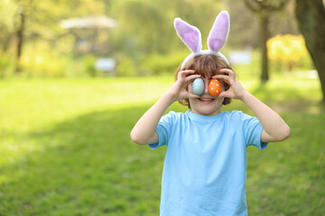 Easter celebration. Cute little boy in bunny ears covering eyes with painted eggs outdoors, space...