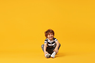 Happy little boy dancing on yellow background. Space for text