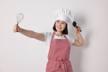 Happy confectioner with whisk and spatula on light grey background