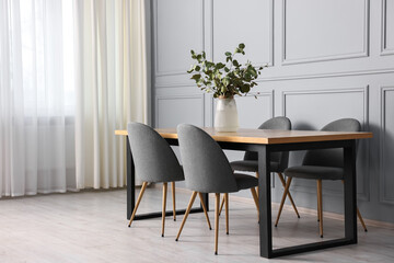 Soft chairs, table and vase with eucalyptus branches in stylish dining room