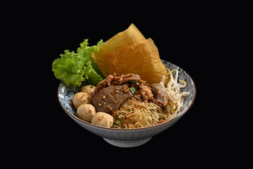 Spicy egg noodles with sliced braised beef, meatballs and vegetables in a bowl on black background. Thai noodle