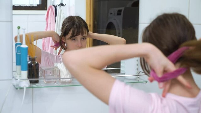Cute teenager girl child doing a ponytail with hair tie looking in the mirror.