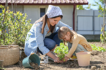 Mother and her cute daughter planting tree together in garden