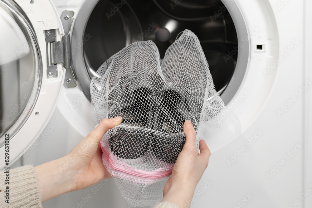 Poster Woman putting stylish sneakers into washing machine, closeup