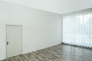 Empty room with brick wall, large window and white door