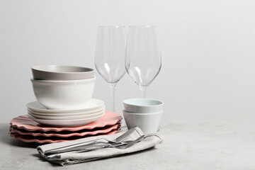Beautiful ceramic dishware, glasses and cutlery on light grey table, space for text
