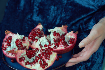 Hands holding a fresh pomegranate on a blue plate. Close-up shot with rich colors and textures....