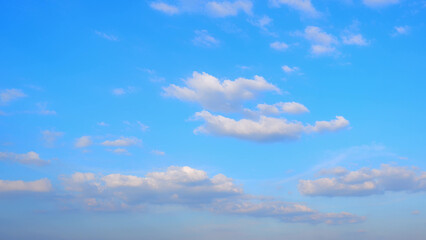 A vivid blue sky scattered with fluffy white clouds. The clouds are spread unevenly, adding a...