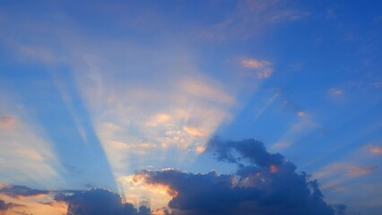 A stunning sunset with the sky displaying beautiful rays of sunlight piercing through scattered clouds. The clouds are tinged with hues of gold and pink. Sunset sky background.
