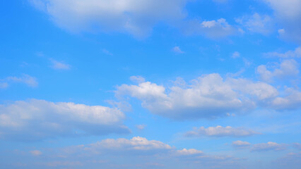 A bright blue sky dotted with fluffy white clouds, creating a serene and calm atmosphere. The clouds vary in size, adding depth and texture to the otherwise clear sky. Nature background.

