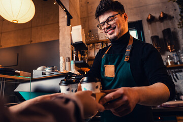 Barista gives takeaway coffee in paper cups to customers in a cafe.