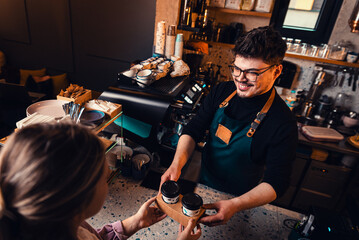 Barista gives takeaway coffee in paper cups to customers in a cafe.