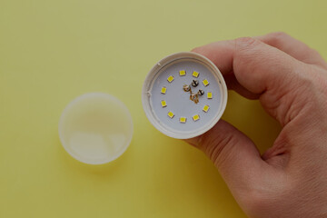 A disassembled burned-out LED lamp in hand on a yellow background, lamp damage, LED lamp repair,...