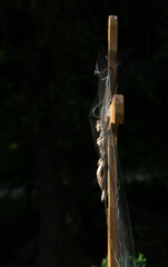 A wooden cross stands against a dark background in the cemetery. On the cross is a statue of Jesus...