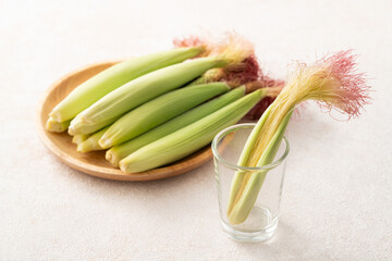 Raw baby corn in husk with red silk on gray table background.