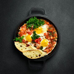 Tasty Breakfast Shakshuka in an Iron Pan. Fried eggs with tomatoes. On a black stone background.