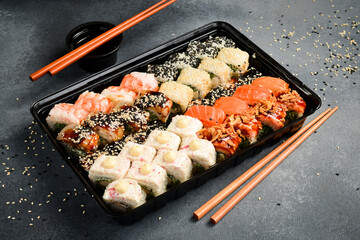 A large set of colored sushi and rolls in a plastic box. Japanese food. Food delivery. close up