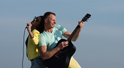 Enjoy music together. Happy young couple hipsters singing with microphones and guitar. Excited...