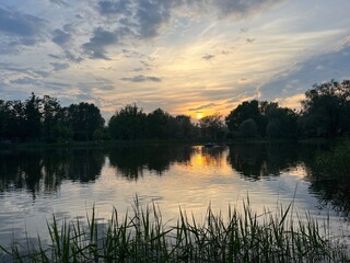 Obraz premium beautiful evening sky with clouds reflection on the lake surface, lake in the park, summer, trees silhouettes reflection