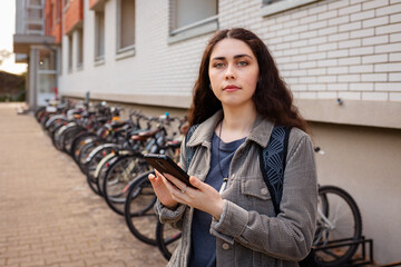 Portrait of young Caucasian woman uses her smartphone to rent bike through app. Free municipality...