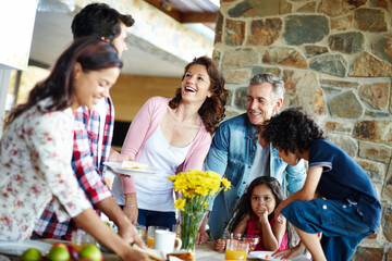 Family, generations and children in dining room with plate, serving and conversation at lunch in home. Men, women and kids with smile, laugh or chat with care at brunch for reunion with love in house